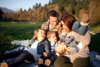 Picture of a family (2 adults and 3 kids) taking a break from life to sit together and play in a quiet field