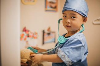 Image of a young child dressed up as a doctor, using a toy stethoscope on a stuffed animal.