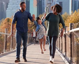 A young successful couple dressed casually and taking their daughter for a walk, lifting her up as they cross over a bridge.